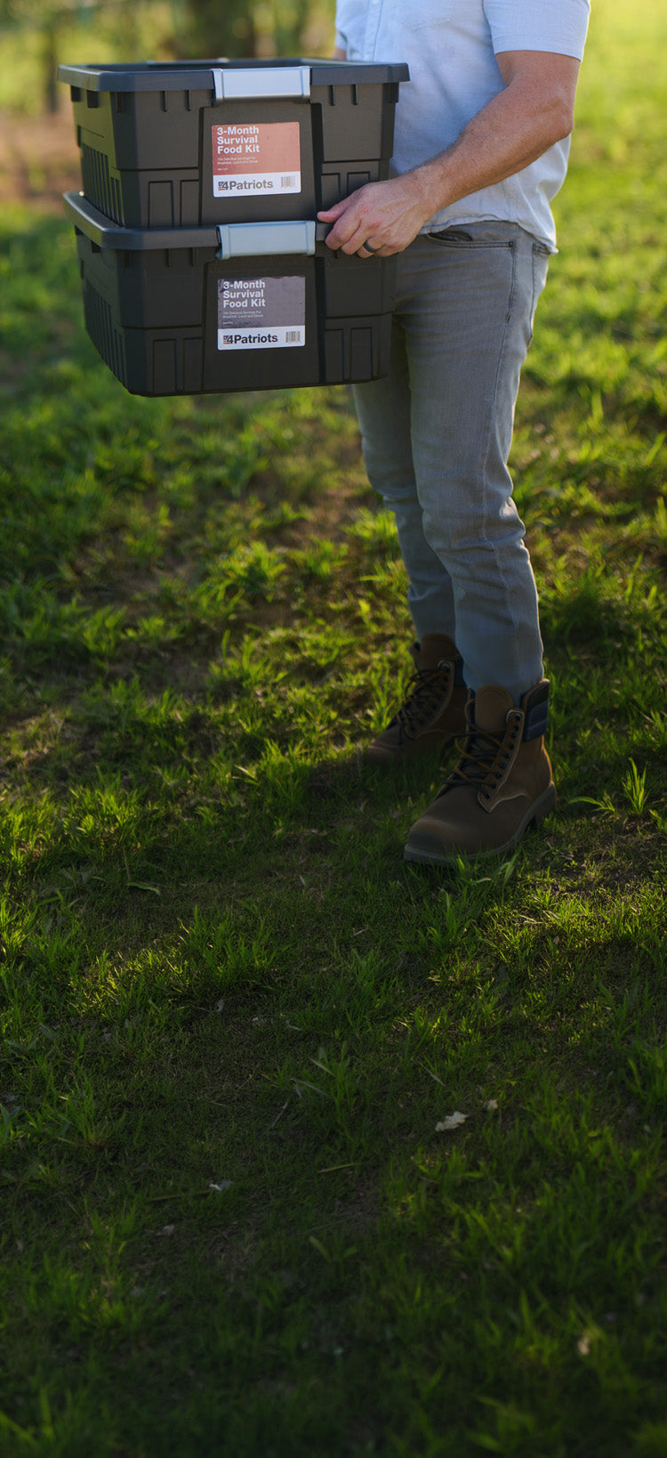 Translation missing: en.3-Month Emergency Survival Food Kit: tall crop of a man carrying two stacked black storage totes through a sunlit field at sunset, emergency food kit
