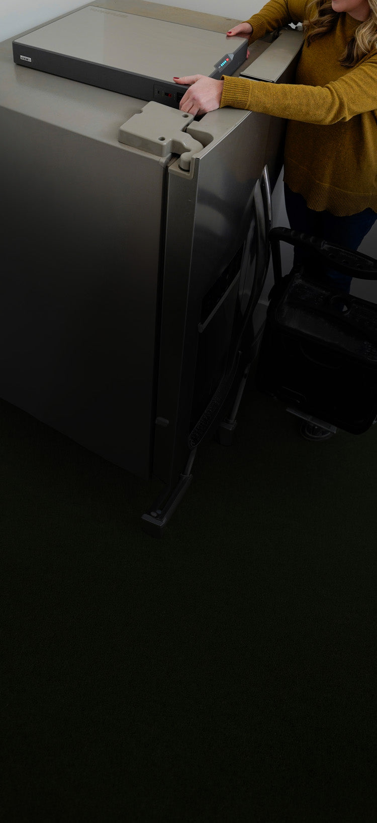 Translation missing: en.Vertical view of the Blackout Buddy Emergency Power Supply on top of a refrigerator with its side outlets in reach, a slim plug-in battery backup unit
