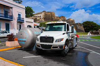 A water tanker truck parked on a street in Old San Juan with a historic fort behind it