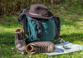 A packed backpack, hiking boots and hat resting on grass beside a map
