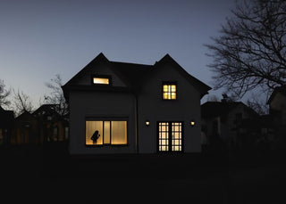 A house at dusk in near-darkness with light showing in only two windows