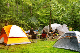 Tents pitched among trees at a wooded campground with campers seated nearby