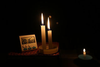 Two lit candles beside a digital clock in a dark room