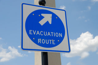 A blue and white evacuation route sign against a blue sky