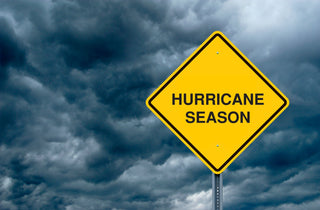A yellow Hurricane Season road sign against heavy storm clouds