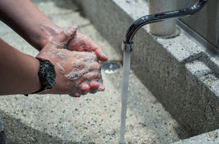 Soapy hands being washed under an outdoor tap