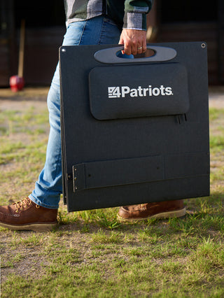 Man in work boots carries the folded 200-Watt Portable Folding Solar Panel by its handle across a farm at sunset, portable off-grid emergency solar power