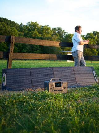 200-Watt Portable Folding Solar Panel unfolded in a farm field at sunset charging a Patriot Power Generator 2200X, with a man nearby for off-grid emergency backup power