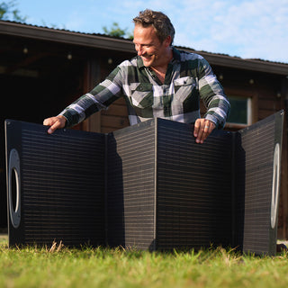 Man sets up the fully unfolded 200-Watt Portable Folding Solar Panel on farm grass outside a barn, harnessing sunlight for off-grid emergency backup power