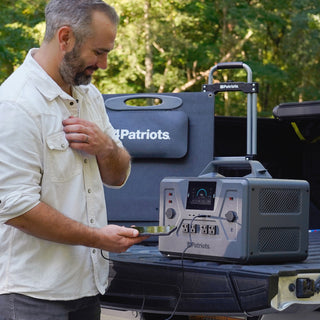 200-Watt Portable Folding Solar Panel and Patriot Power Generator 2200X on a truck tailgate as a smiling man checks his phone charging at 98%, portable off-grid emergency power