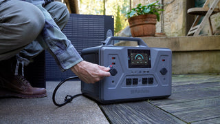 Hand plugging the 200-Watt Portable Folding Solar Panel cable into a Patriot Power Generator 2200X on a patio, quick tool-free setup for off-grid emergency backup power