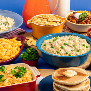 3-Month Emergency Survival Food Kit: prepared meals across a blue table with creamy pasta, mac and cheese, chili, banana chips and pancakes, survival food
