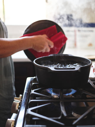 Hand lifting a lid off a pot of boiling water on a gas stovetop to prepare a 72-Hour Emergency Survival Food Kit meal, easy just-add-water survival food