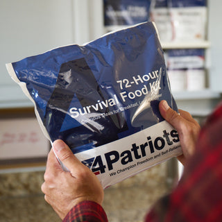 Man in flannel holding a 72-Hour Emergency Survival Food Kit pouch in a kitchen with more kits stocked behind, long-term food storage