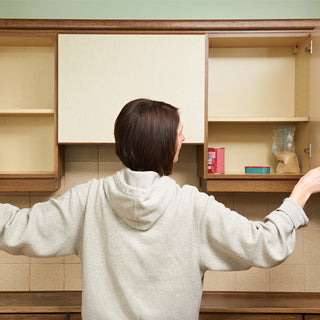 Woman opening nearly empty kitchen cabinets, showing why a 72-Hour Emergency Survival Food Kit and long-term food storage matters