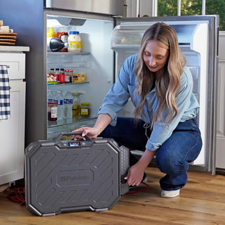 Woman kneeling by an open refrigerator connects the Patriot Power Solar Generator AlphaCase Elite for kitchen power outage home backup