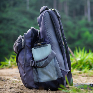 Aqua-Bright 2-in-1 Water Bottle & Lantern tucked into a backpack side pocket on a forest trail, compact water bottle and survival gear for hiking