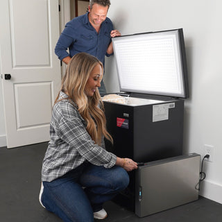 Couple at a garage chest freezer powered by the Blackout Buddy Emergency Power Supply plugged in beside it, backup power that protects frozen food in an outage