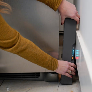 Woman sliding the Blackout Buddy Emergency Power Supply onto the floor beside a garage refrigerator, plug-in battery backup that keeps the fridge running in an outage