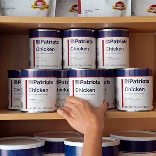 Hand takes a 28 oz 4Patriots Chicken can from a stocked pantry shelf, showing how the Ultimate Chicken Meat Jumbo Can supply stores at home.