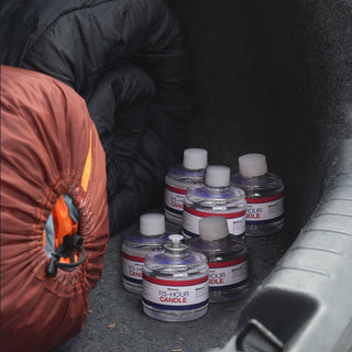 Six 115-hour candles in a car trunk beside a rolled orange sleeping bag and a black quilted blanket