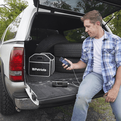 Man sitting in his trunk using his Patriot Power All-in-1 Emergency Car Kit to charge his cellphone.