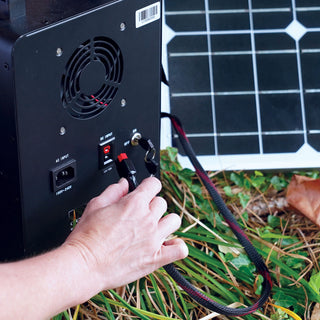 25-Foot Solar Panel Extension Cord being plugged into a portable power station's DC input beside a solar panel outdoors on the grass