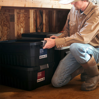 Man stacking 4Patriots 3-Month Survival Food Kit totes in a basement, long-term food storage tucked into unfinished space