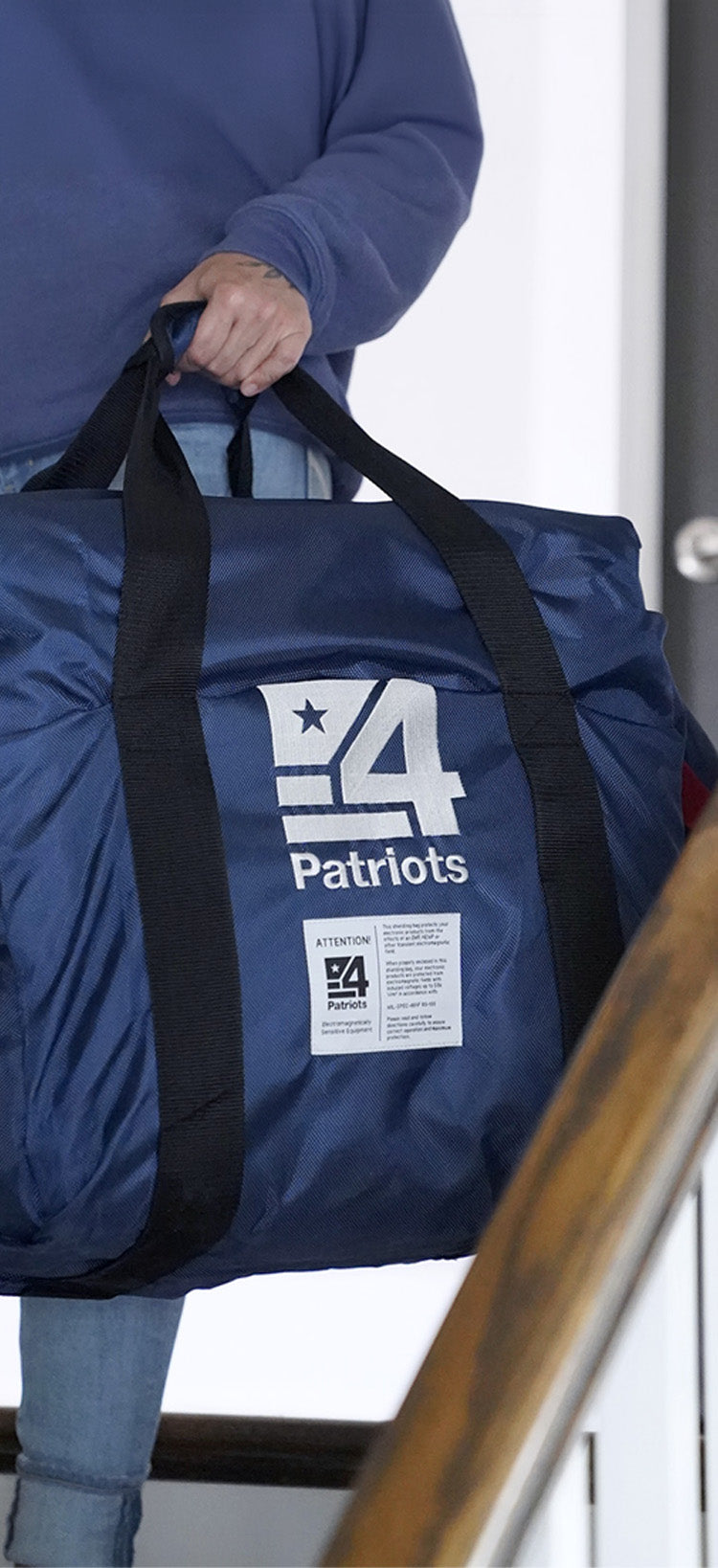 Translation missing: en.4Patriots EMP Shielding Bag, a navy Faraday-style bag with the 4Patriots logo and a caution label, carried down a staircase to protect sensitive electronics for disaster preparedness