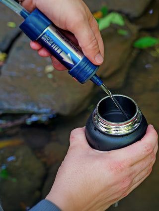 Family Emergency Essentials Package close-up of the blue Patriot Pure Water Filter dispensing clean filtered water into a bottle for emergency water filtration off-grid