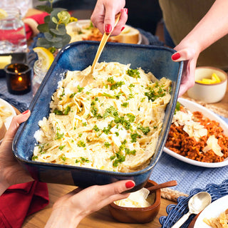 Hands pass a blue dish of creamy stroganoff made from the Family Favorites Emergency Survival Food Package at a set dinner table.