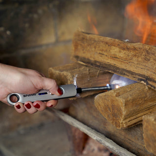 Hand using the 4Patriots Freedom Flame Rechargeable Flexible Arc Lighter to ignite kindling beneath logs in a fireplace, survival gear