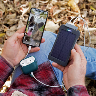 Food, Power & Light Emergency Go-Bag Starter Package PPC-CX portable solar power bank charging a man's phone and earbuds outdoors on fall leaves, off-grid emergency charging