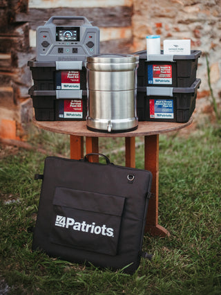 Gold Reserve Emergency Survival Package: generator, water filter, food kit totes and solar panel case displayed together on a table outside a cabin, emergency survival kit