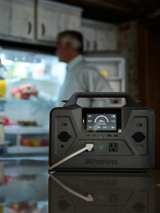 Gold Reserve Emergency Survival Package: Patriot Power Generator 1200 on a counter powering a refrigerator as a man loads it, power outage backup