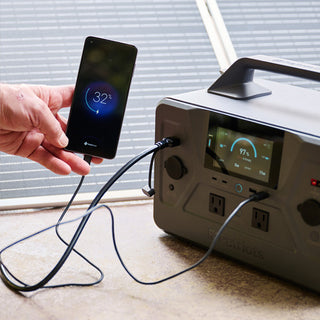 Gold Reserve Emergency Survival Package: hand charging a cell phone plugged into the Patriot Power Generator 1200 portable solar generator, emergency preparedness