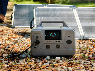 Gold Reserve Emergency Survival Package: Patriot Power Generator 1200 charging outdoors on gravel with two 100W folding solar panels behind it, off-grid power