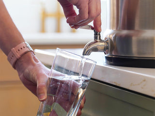 Gold Reserve Emergency Survival Package: close-up of a hand pouring filtered water from the Ultimate Water Filter spigot into a glass, clean drinking water