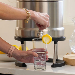 Gold Reserve Emergency Survival Package: Ultimate Water Filter on a counter dispensing water from the spigot into a lemon-garnished glass, emergency water filter