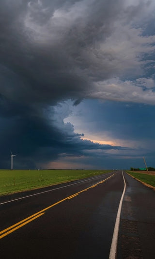 Dark storm clouds gathering over an empty rural highway and wind turbine at dusk, a dramatic severe-weather scene evoking power outages and disaster preparedness