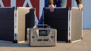 Patriot Power Solar Generator 2200X power station charging from two 100W folding solar panels as a man sets them up by a barn, off-grid emergency backup power