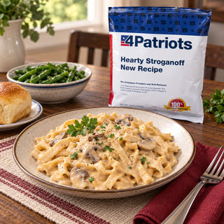 Hearty Stroganoff Pouch behind a plate of creamy mushroom noodles with parsley, a dinner roll and green beans on a kitchen table, survival meals