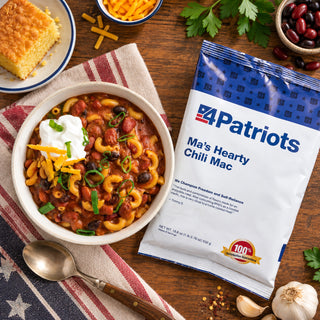 Overhead of Ma's Hearty Cheesy Chili Mac Pouch beside chili mac topped with sour cream, cheddar and scallions, with cornbread, beans and garlic, survival food