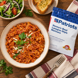Top-down view of Nonna's Best Lasagna-Style Marinara Pouch with a bowl of ruffled pasta in tomato sauce, shaved parmesan, garlic bread and a fork, survival food