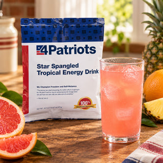 Star-Spangled Tropical Energy Drink Pouch upright next to a tall iced pink drink with grapefruit, pineapple and orange in sunlight, survival food