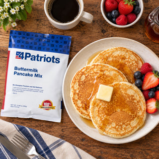 Buttermilk Pancake Mix Pouch flat-lay next to buttered pancakes with syrup and mixed berries and a cup of black coffee, an emergency food breakfast