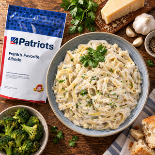 Frank's Favorite Alfredo Pouch overhead with a blue bowl of fettuccine alfredo, a parmesan wedge, garlic cloves, fresh parsley, broccoli and crusty bread, emergency food