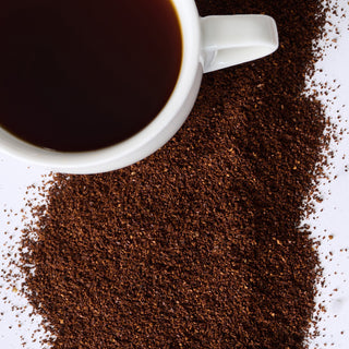 Freedom Joe Survival Coffee Pouch shown as a steaming white mug of black coffee amid scattered coffee grounds, a survival food staple
