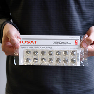 Hands holding a sealed IOSAT Potassium Iodide Tablets 130mg package showing the full blister pack of 14 tablets through clear packaging
