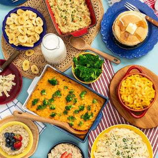 4-Week Survival Food Kit meals in an overhead flatlay: cheesy broccoli casserole, mac and cheese, pancakes, creamy pasta, oatmeal with berries and banana chips, hearty long-term food storage